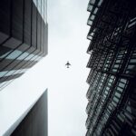 A dramatic view of an airplane flying above modern skyscrapers in London, UK.