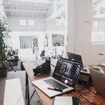 A bright, modern workspace featuring laptops, a camera, and a drawing tablet in an indoor office.